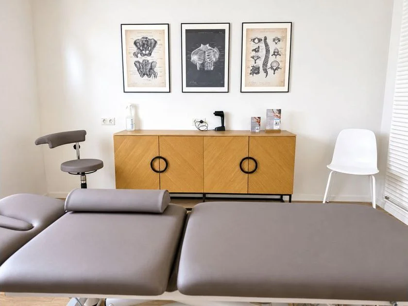 Behandlungsraum mit Therapieliege, Anatomie-Bildern und Sideboard.
